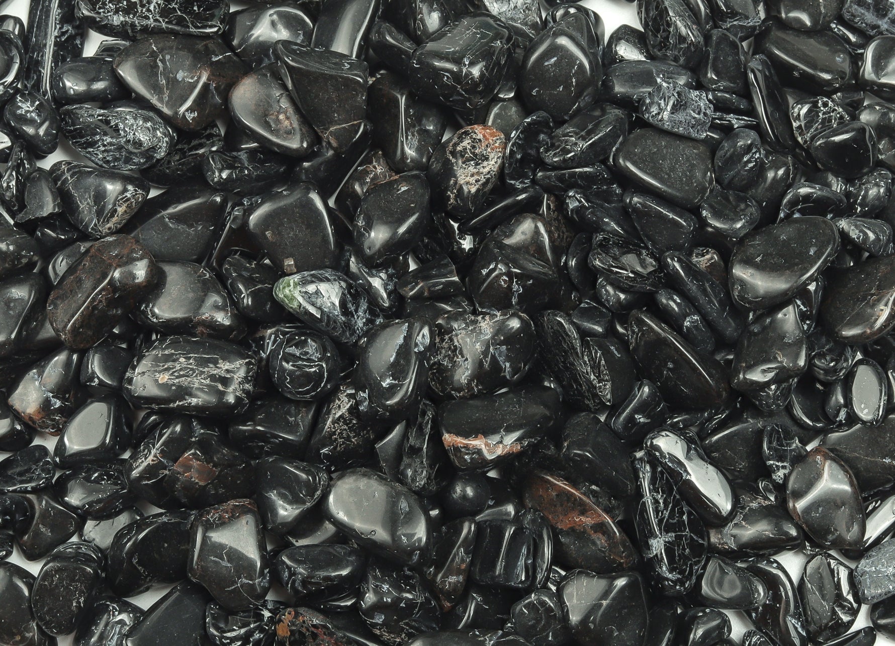 Black tourmaline crystal chips in semi-tumbled 7-12mm size, shown in bulk with irregular black stone pieces from GemstoneGO