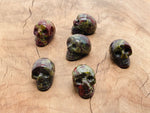Carved Dragon Blood Jasper skull gemstone, 25mm, showing detailed red and brown natural stone patterns and smooth polished surface.