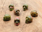 Unakite skull carved gemstone, 25mm, showing detailed green and pink mineral patterns on a polished surface.