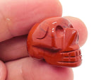 Red Jasper skull carved gemstone, 25mm, from GemstoneGO, showing detailed carved facial features and vibrant red color.