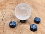 Sodalite crystal sphere on a carved gemstone stand, used as elegant home decor piece with blue and white natural stone patterns.