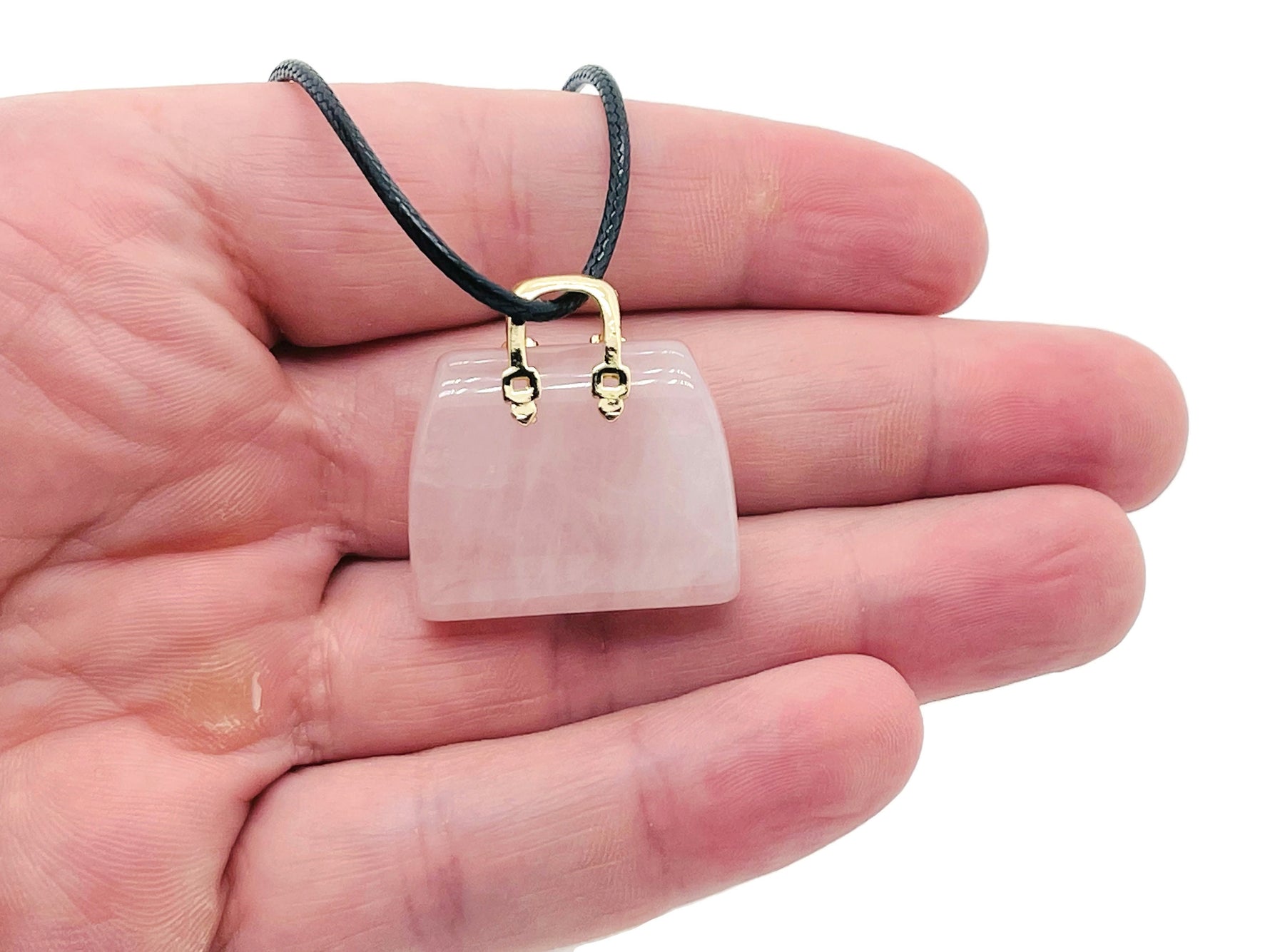 Rose quartz crystal carved into a handbag pendant, showcasing a smooth, pink gemstone with intricate detailing in the image.