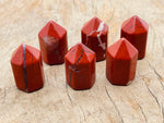 Red Jasper obelisk tower crystal, 25mm, from GemstoneGO, showcasing a polished red gemstone with natural patterns and smooth faceted surfaces.