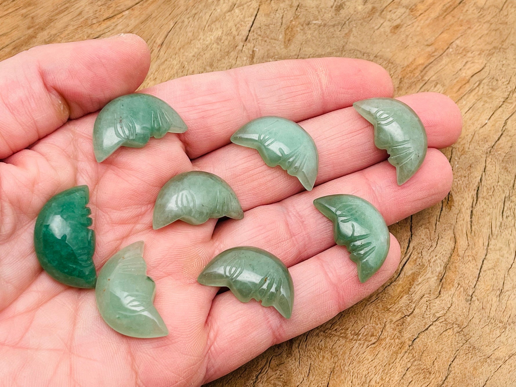 A 25mm Aventurine crystal moon face gemstone with carved smile design, showcasing a smooth, polished surface and natural green hue.