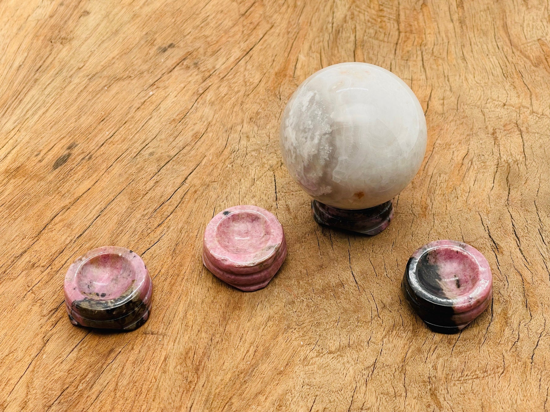 Rhodonite crystal sphere on a carved gemstone stand, used as elegant home decor piece showcasing pink and black gemstone patterns.