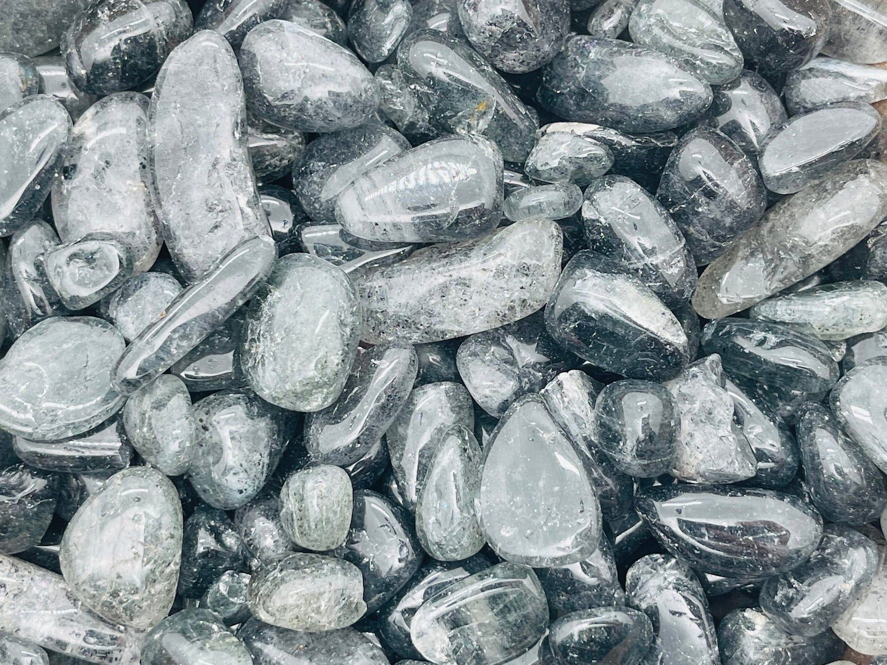 Black strawberry quartz crystal chips, semi-tumbled stones from GemstoneGO, 7-18mm, shown in bulk with smooth, polished surfaces.