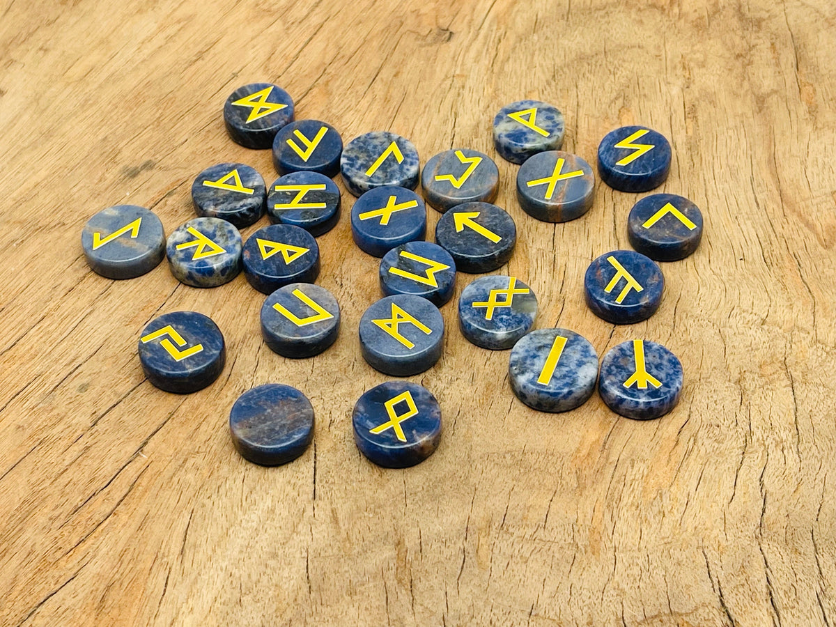 Set of 25 sodalite crystal rune stones engraved with Elder Futhark alphabet, arranged in a crystal kit for divination.