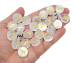 Set of 25 clear quartz crystal rune stones engraved with Elder Futhark runes, arranged in a row on a white surface.