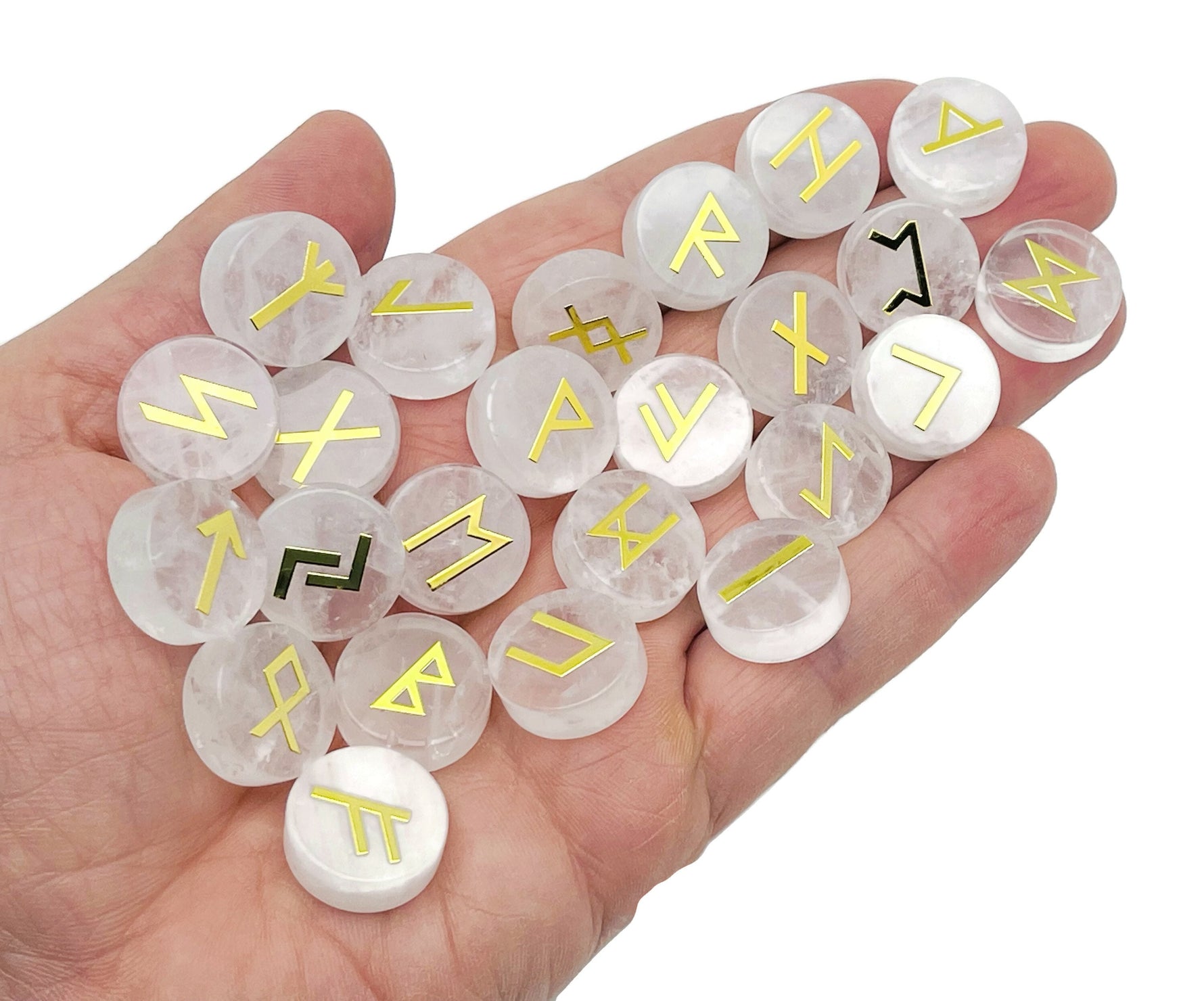 Set of 25 clear quartz crystal rune stones engraved with Elder Futhark runes, arranged in a row on a white surface.