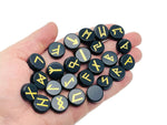 Set of 25 obsidian crystal rune stones engraved with Elder Futhark alphabet, arranged in a crystal kit for divination and rune reading.