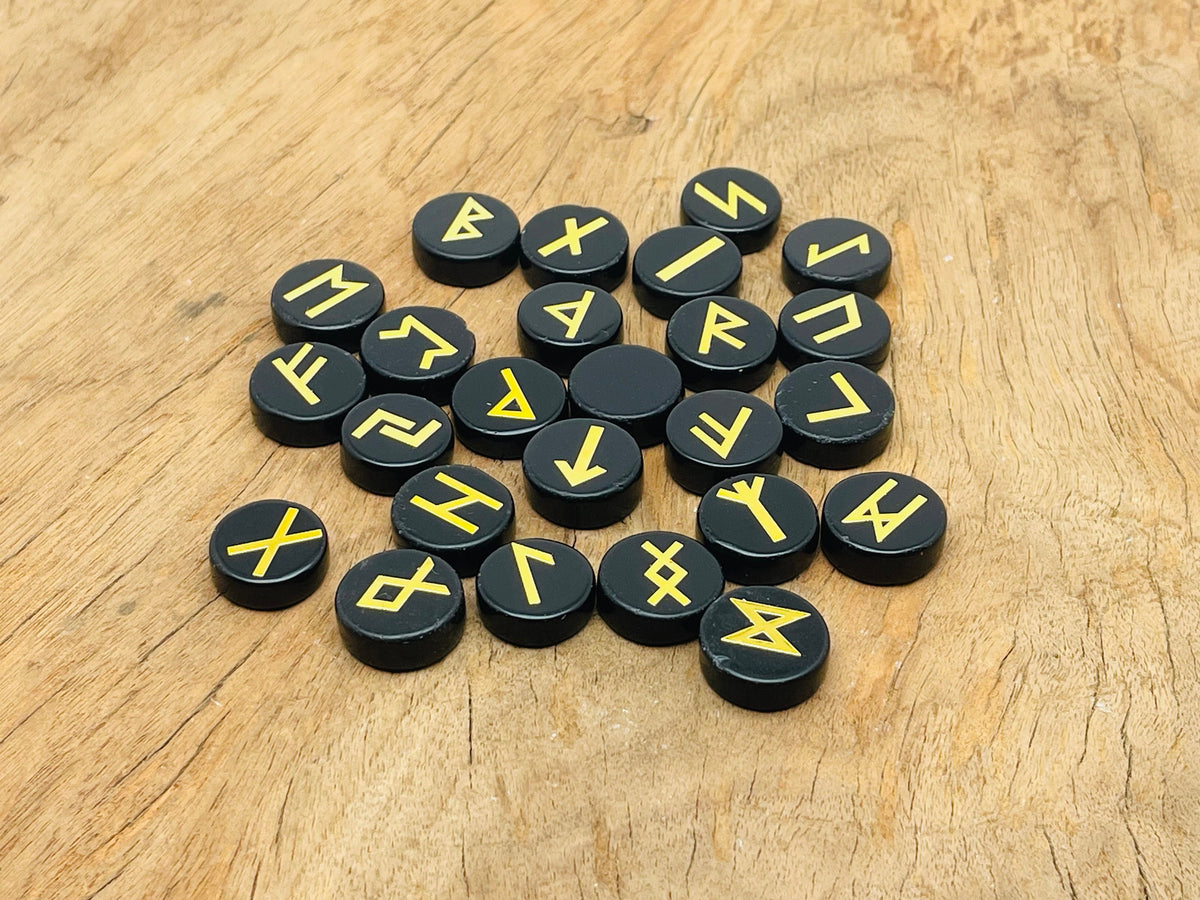 Set of 25 engraved obsidian crystal rune stones with Elder Futhark alphabet from GemstoneGO, arranged on a neutral background.