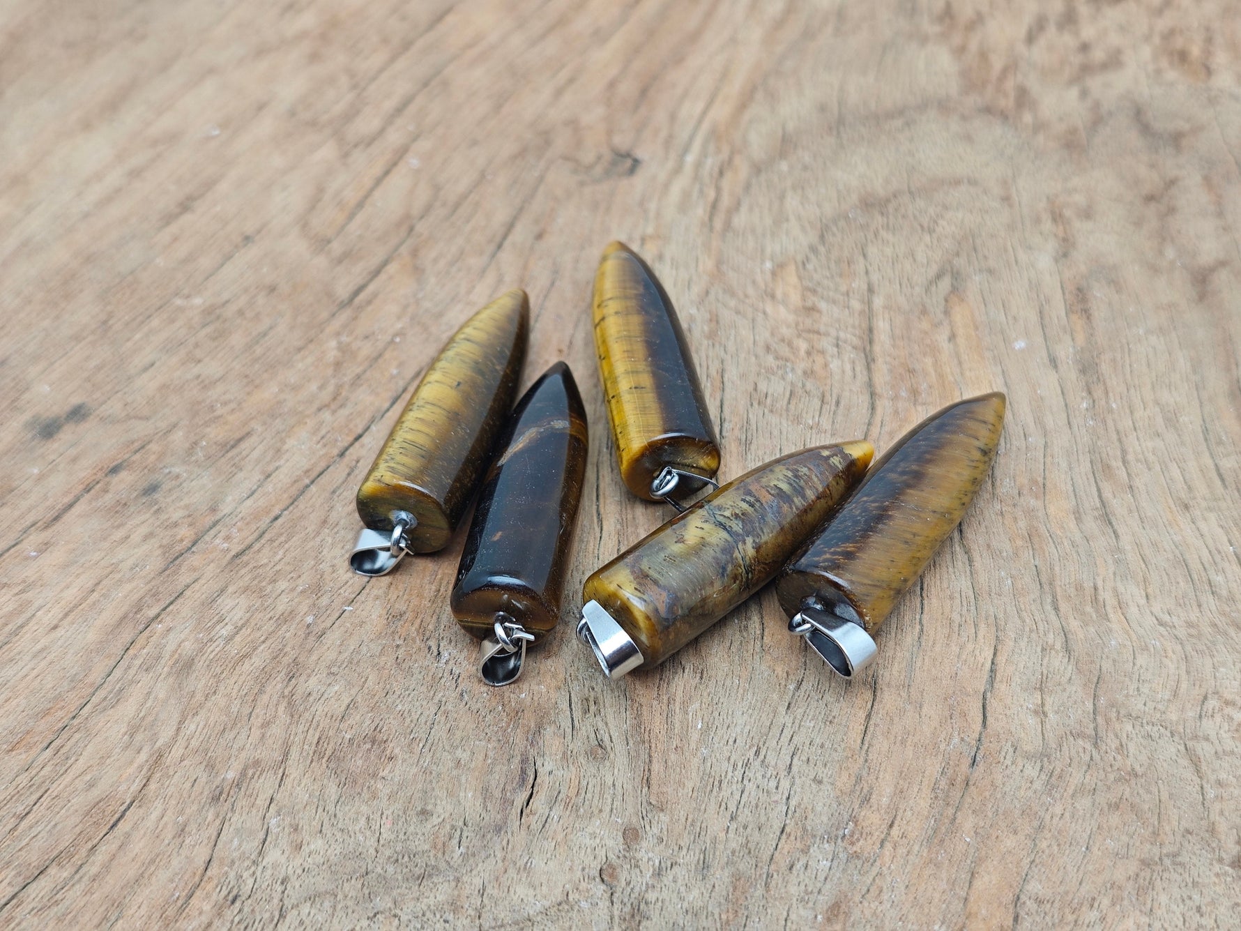 Polished tiger eye bullet gemstone pendant with carved design, featuring natural golden-brown hues and smooth, rounded shape.