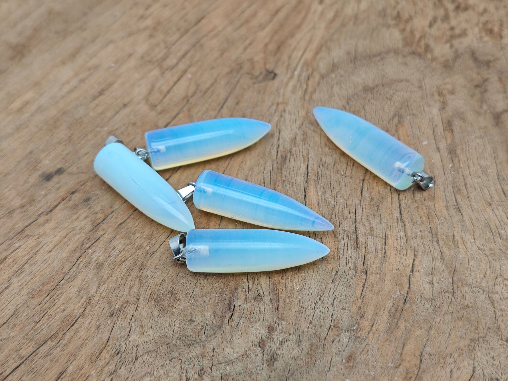 Polished opalite bullet gemstone pendant with carved details, showcasing smooth, reflective surface and natural stone beauty.