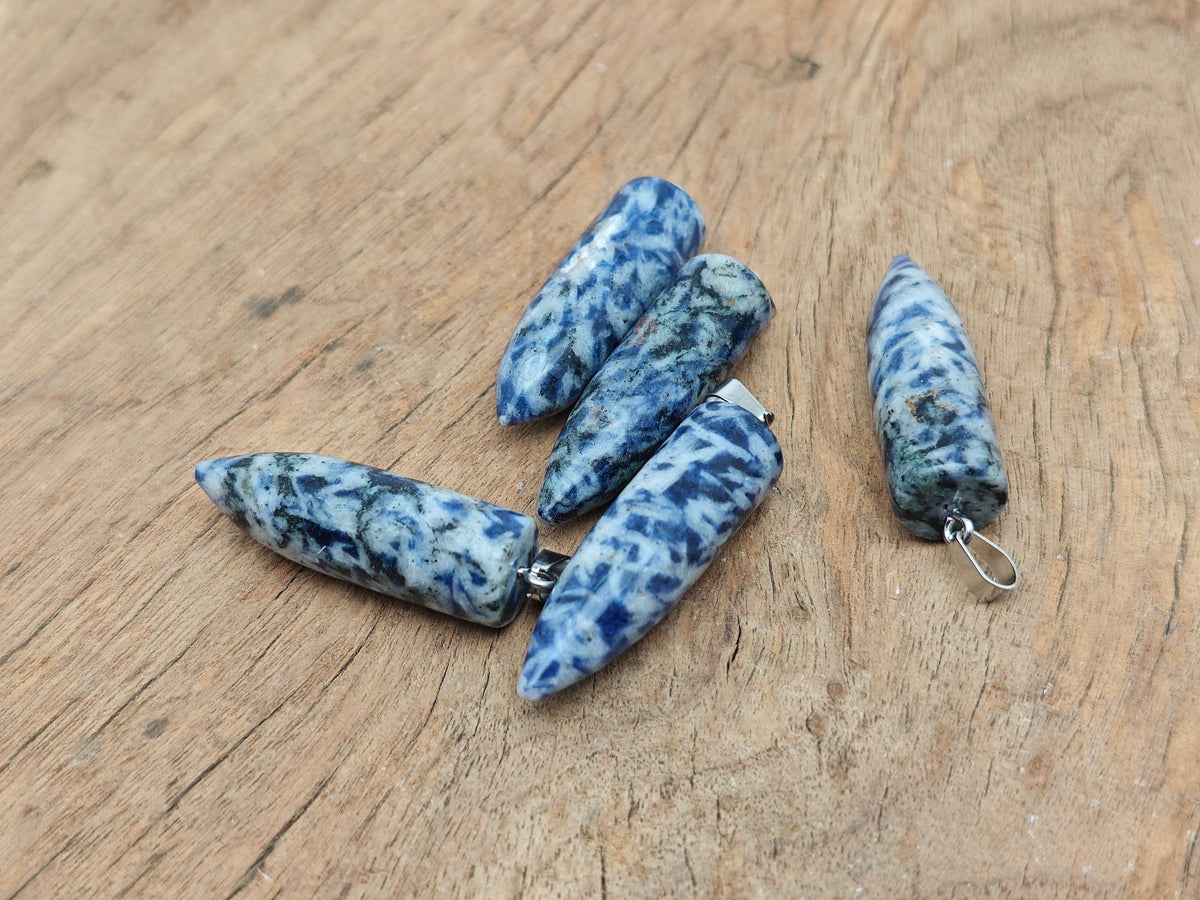 Polished blue spot jasper bullet gemstone pendant with carved details, featuring a natural gemstone shape and vibrant blue and brown patterns.