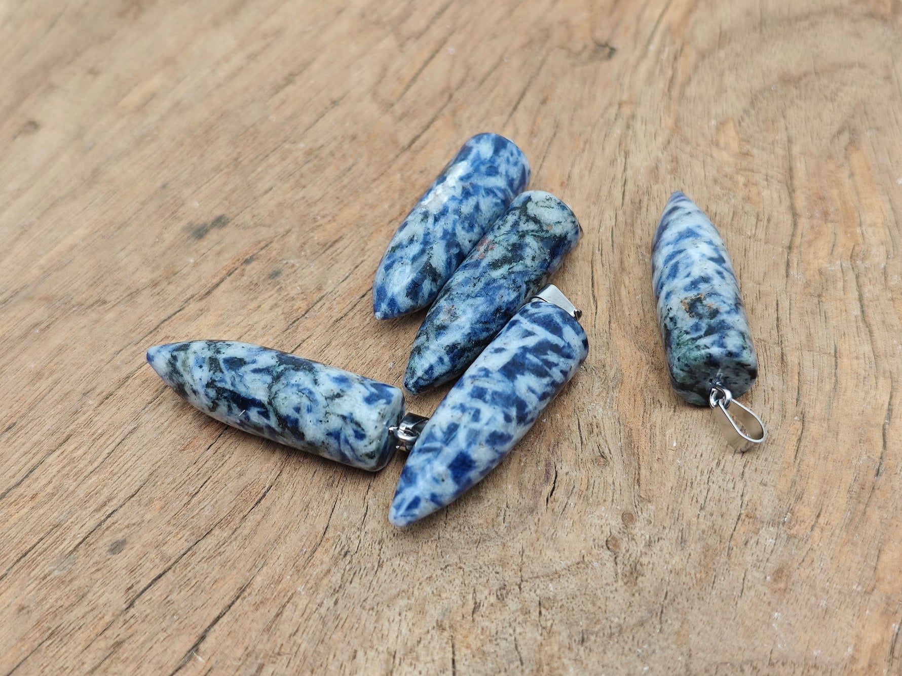 Polished blue spot jasper bullet gemstone pendant with carved details, featuring a natural gemstone shape and vibrant blue and brown patterns.