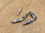 Polished Rhodonite bullet gemstone pendant with carved details, showcasing a smooth, vibrant pink and black stone on a neutral background.