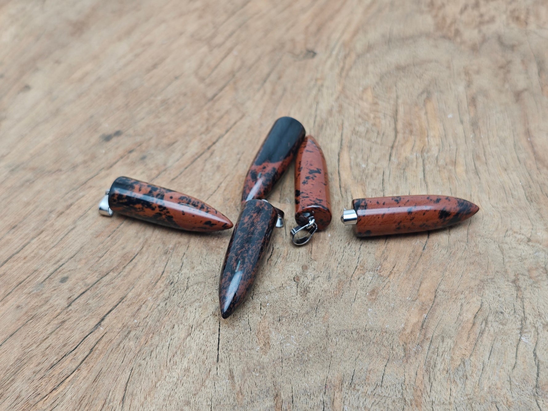 Polished mahogany obsidian bullet gemstone pendant with carved design, hanging from a silver chain, by GemstoneGO.