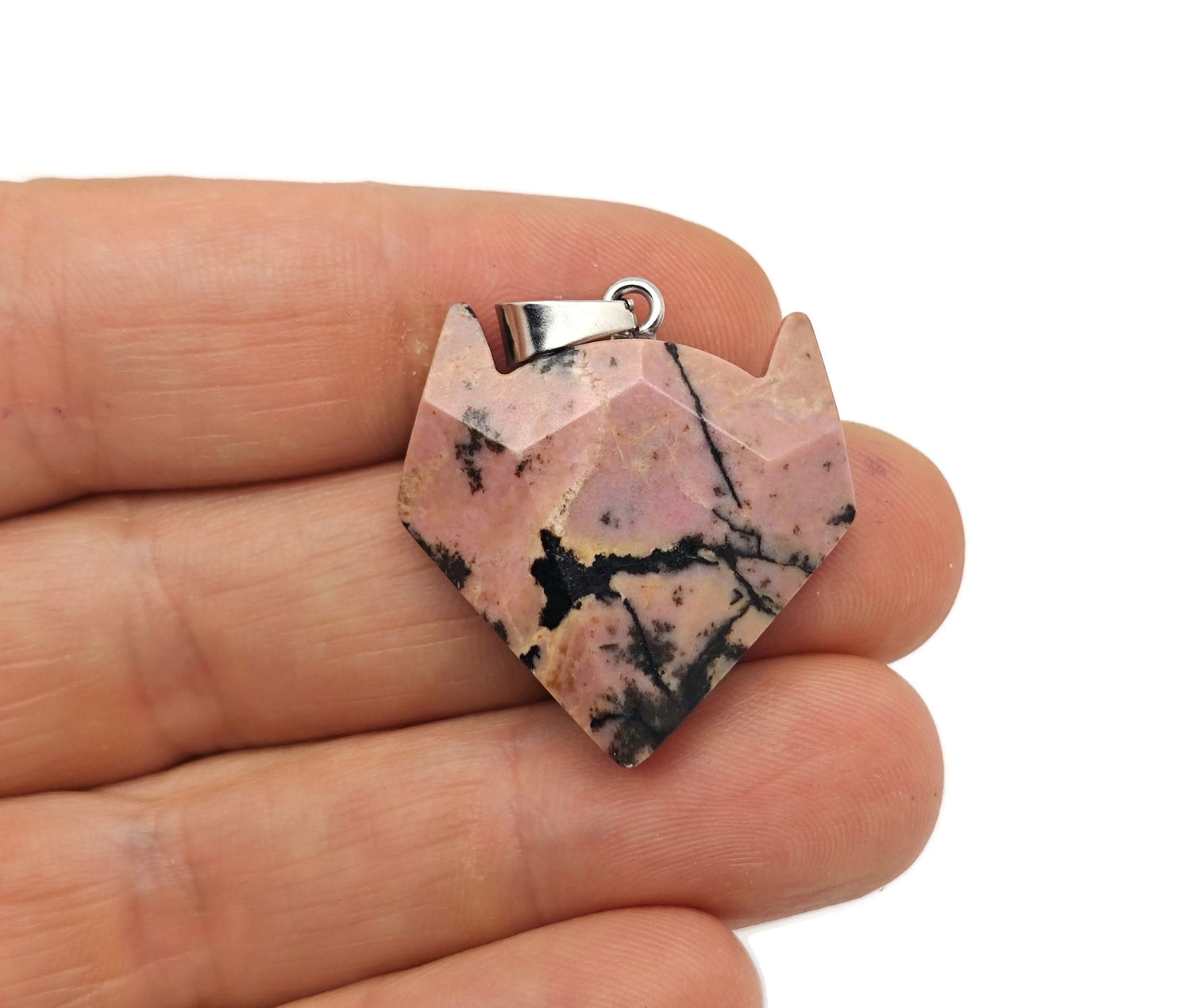 Rhodonite wolf head gemstone pendant hanging on a chain, showcasing intricate carved details and vibrant pink and black colors.