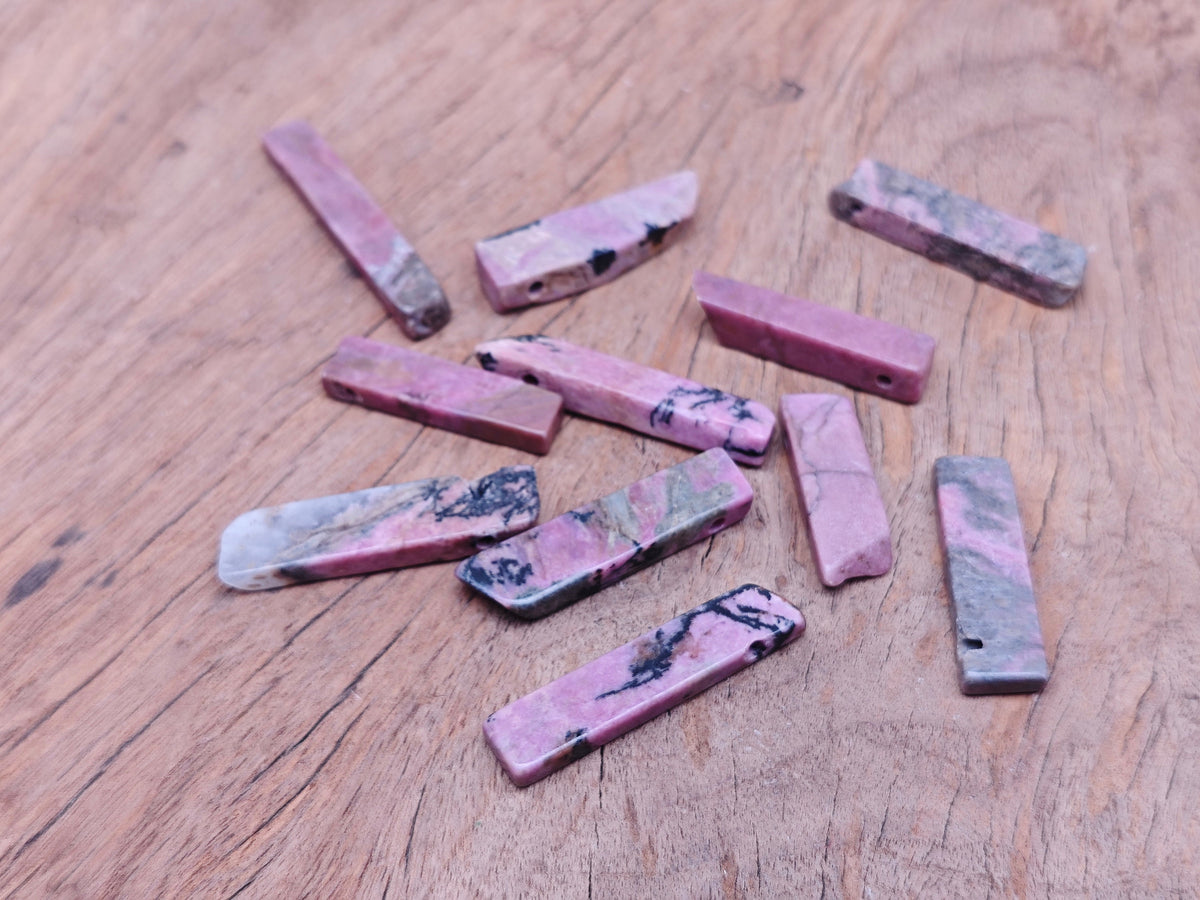 Rhodonite drilled tumbled gemstone pendant from GemstoneGO, showcasing a smooth pink and black patterned stone on a neutral background.