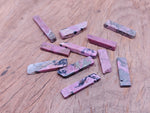 Rhodonite drilled tumbled gemstone pendant from GemstoneGO, showcasing a smooth pink and black patterned stone on a neutral background.
