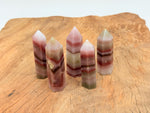 Pink banded calcite obelisk tower crystal from GemstoneGO, showcasing layered pink and white bands with a pointed top.