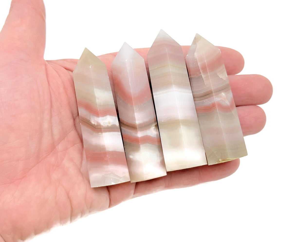 Pink banded calcite obelisk tower crystal from GemstoneGO, featuring soft pink and white striations, standing upright with a polished surface.