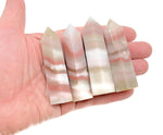 Pink banded calcite obelisk tower crystal from GemstoneGO, featuring soft pink and white striations, standing upright with a polished surface.