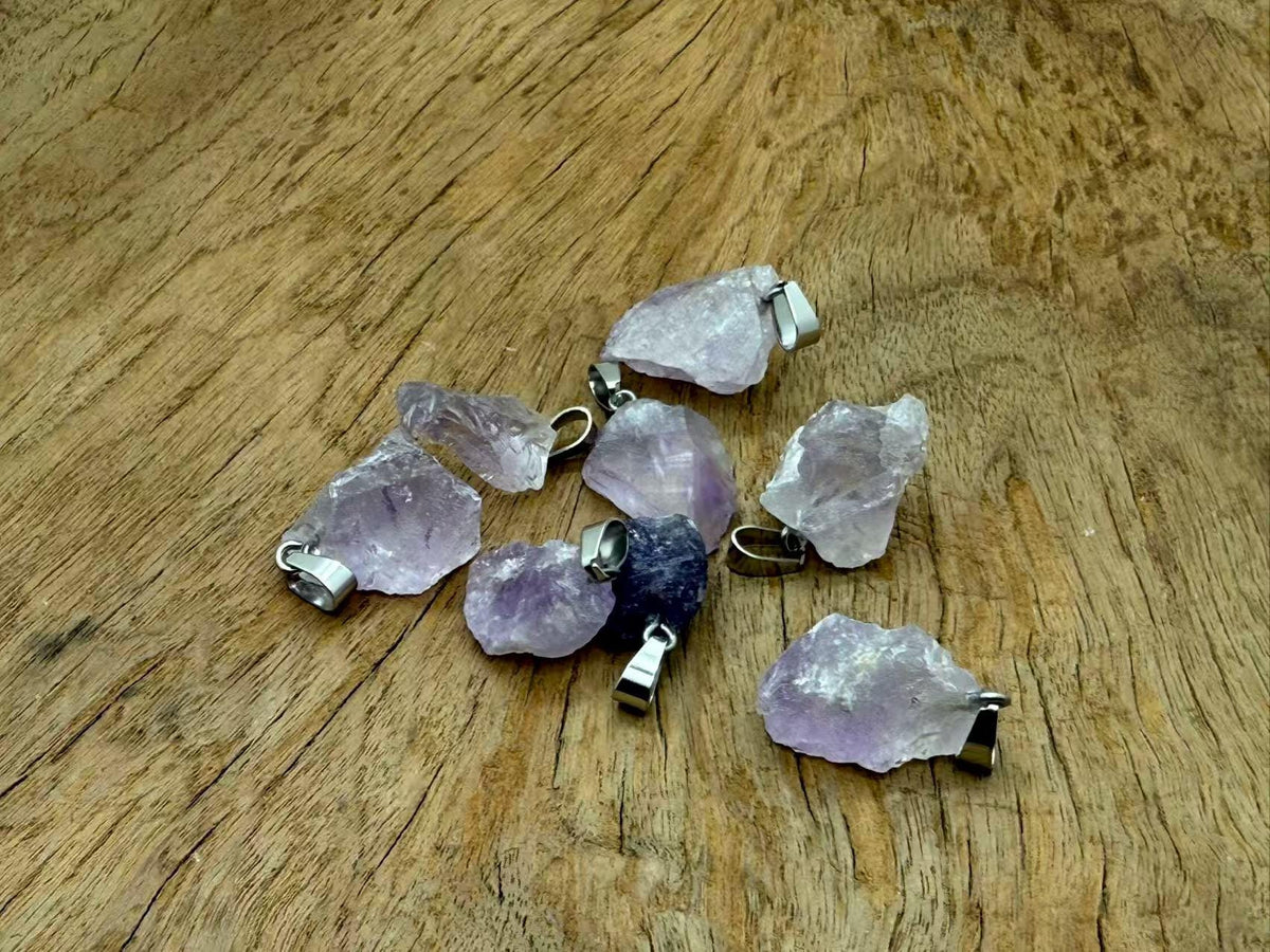 Amethyst crystal pendant from GemstoneGO, showcasing a polished purple gemstone with silver connectors on a jewelry-making display.