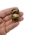Handcrafted tiger eye frog gemstone carving with detailed features, displayed as a small creature statue on a neutral background.